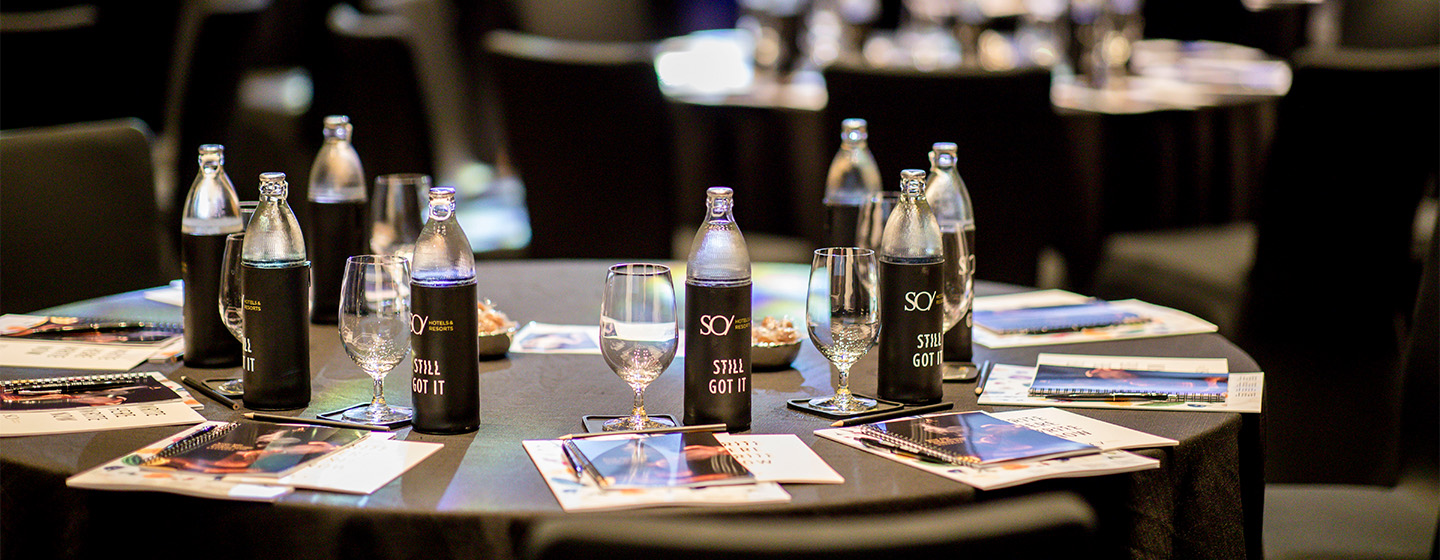 A round table ladened with water bottles, glasses and note books.
