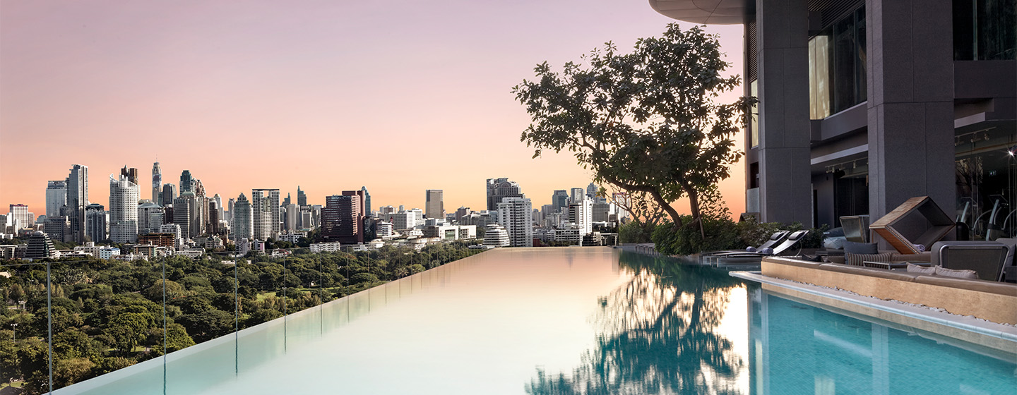 An infinity pools looks over the Bangkok skyline under a pink and purple sunset