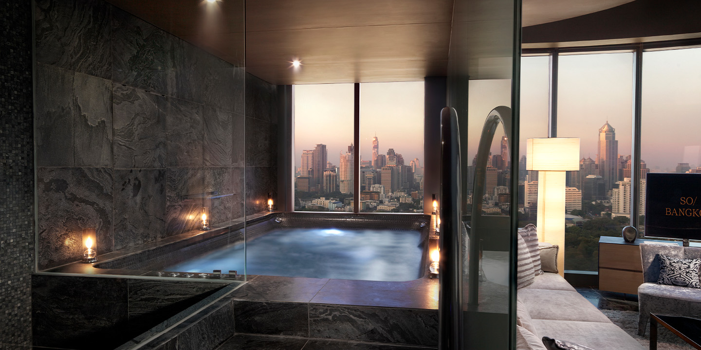 An in-room jacuzzi lined with lit candles and floor to ceiling widows with a skyline view.