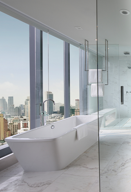 http://A%20large%20bathtub%20sits%20next%20to%20floor%20to%20ceiling%20windows%20displaying%20a%20skyline%20view.%20A%20glass%20divider%20separate%20a%20walk-in%20shower.