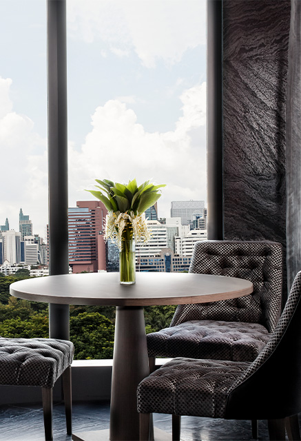http://A%20small%20round%20table%20and%20grey%20chairs%20sit%20next%20to%20a%20window%20overlooking%20Bangkok's%20Lumpini%20Park.