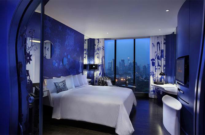 http://A%20blue%20and%20white%20themed%20hotel%20room%20with%20a%20large%20bed,%20desk,%20and%20floor%20to%20ceiling%20window.