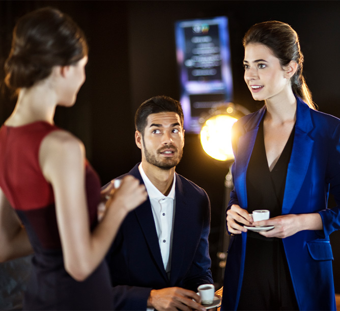 Two women and a man are talking whilst holding espresso cups.