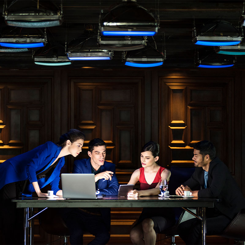 Four people having a meeting sit at a table in a dimly lit meeting room.