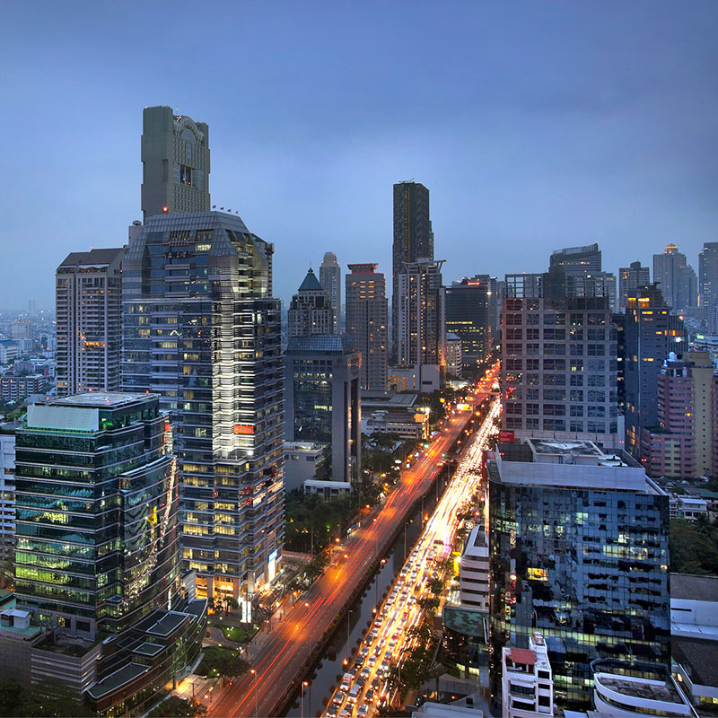 An elevated view of the Bangkok skyline and busy road below at sunset.