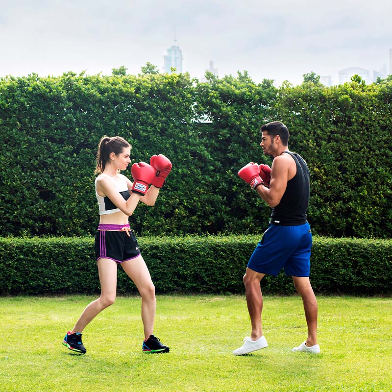 A man and a woman wearing boxing gloves face eachother in a grassy area