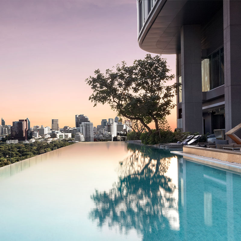 An infinity pools looks over the Bangkok skyline under a pink and purple sunset.