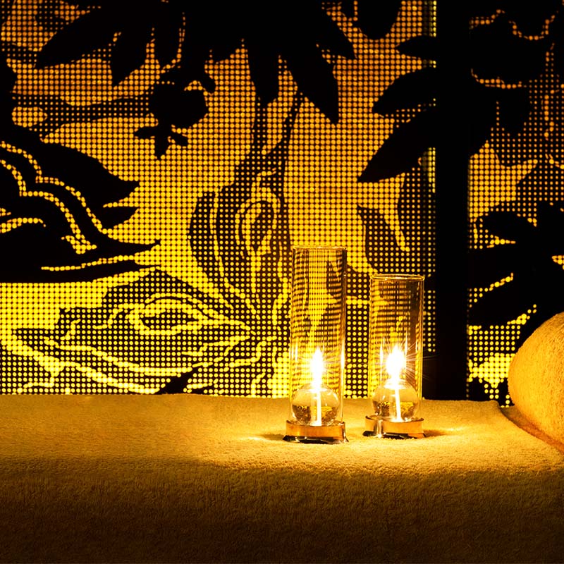 Two candles in glass lamps sit on a massage bed.
