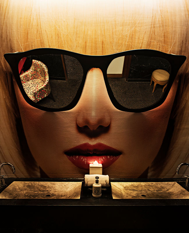A woman with blonde hair wears large black sunglasses reflecting casino chips and cards. Her red lips are highlighted by a lit lighter below, evoking a mysterious, glamorous vibe.