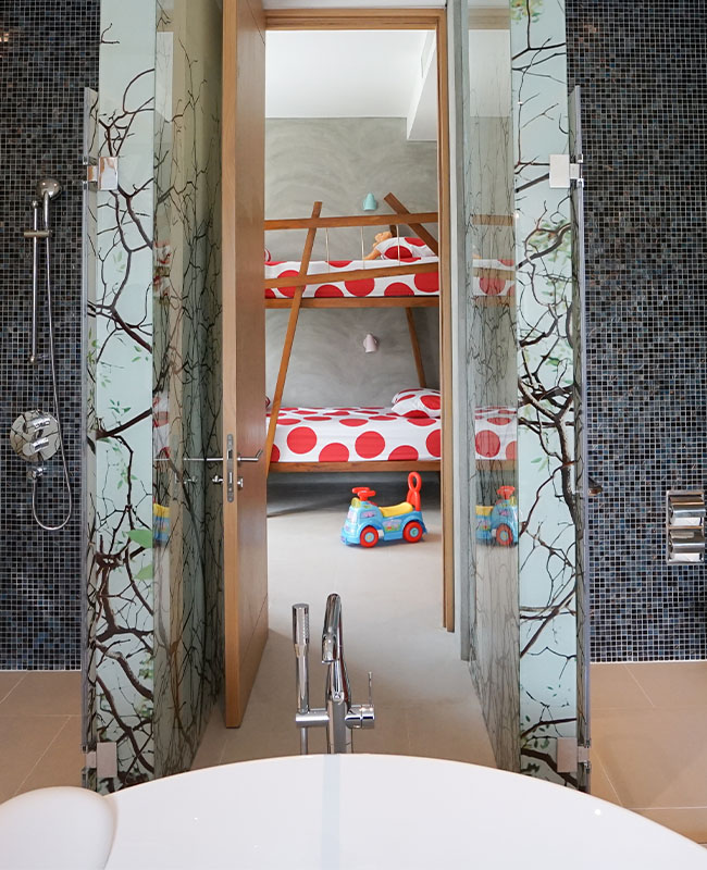 View from a modern bathroom with a freestanding tub, looking into a children's room with bunk beds featuring red polka dot bedding and a toy car.