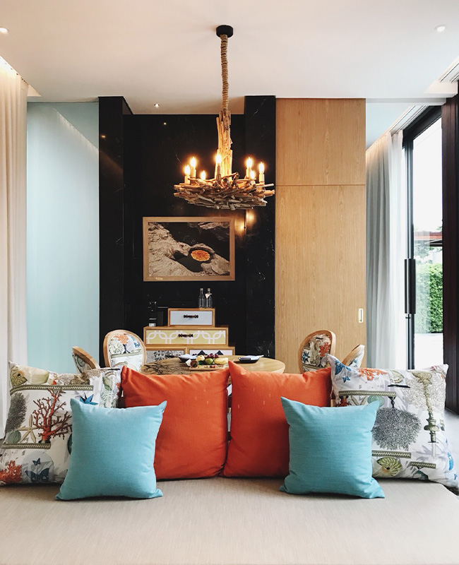 Modern living room with a chandelier, colorful cushions, and large windows allowing natural light to flow in.
