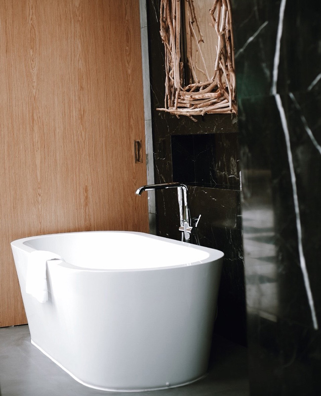A modern bathroom featuring a sleek white freestanding bathtub against a dark marbled wall. A towel hangs over the tub edge, creating a serene and elegant atmosphere.