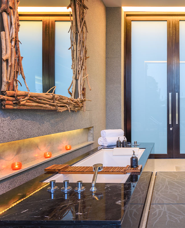Modern bathroom with a sleek black tub, wooden décor accents, and frosted glass doors. Warm lighting and candles create a serene, spa-like ambiance.