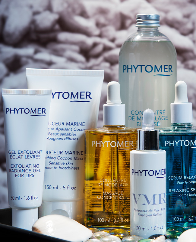 A collection of Phytomer skincare products, including creams and serums, arranged on a surface. The backdrop features soft-focus pebbles, evoking a calm, spa-like ambiance.