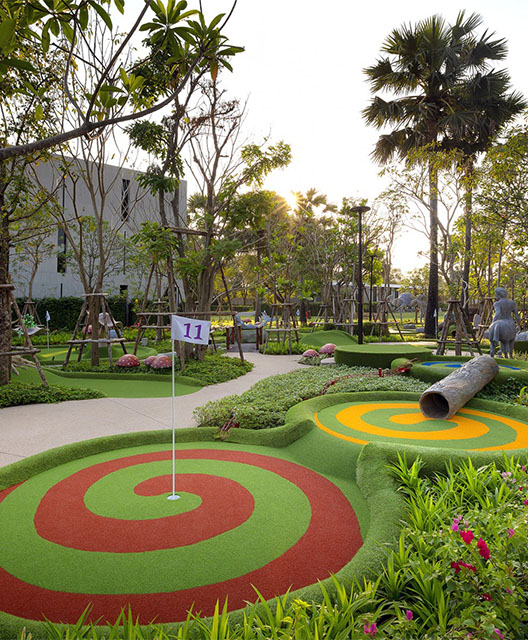 http://Mini-golf%20course%20with%20colorful%20spiral%20patterns,%20lush%20greenery,%20tall%20trees,%20and%20a%20serene,%20sunny%20ambiance%20in%20a%20park%20setting.
