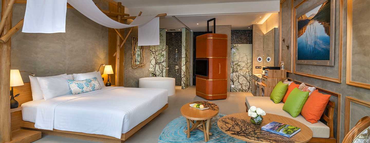 A cozy hotel room features a king-sized bed, vibrant cushions on a sofa, warm lighting, and nature-inspired decor, creating a serene ambiance.