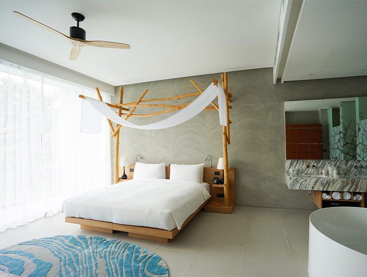 Minimalist bedroom with a canopy bed, white linens, and wooden accents. Soft lighting from sheer curtains creates a serene, calming atmosphere.