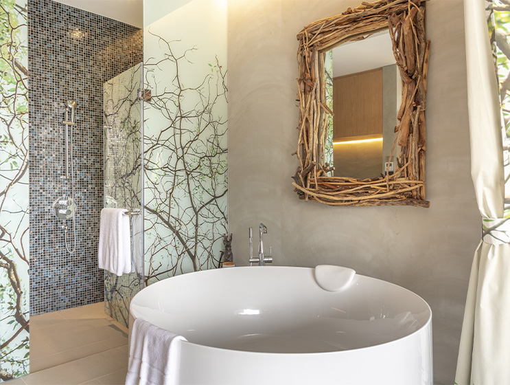 Elegant bathroom with round white bathtub, ornate mirror, and a leafy mural on the wall, creating a serene and luxurious atmosphere.