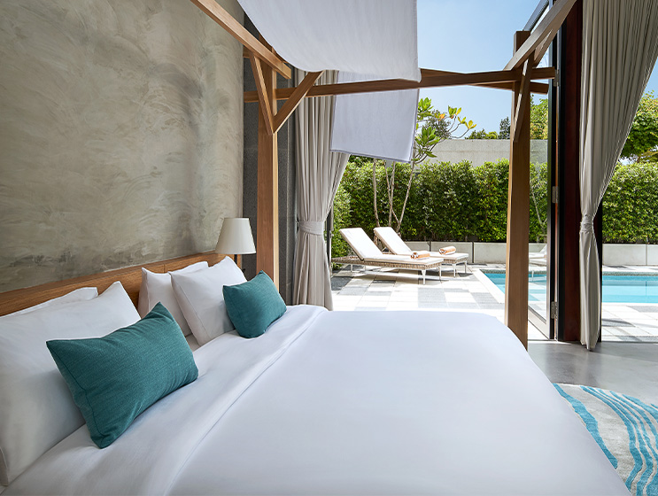 Luxurious hotel room featuring a king-sized bed, modern decor, and a view of a private pool through large windows.