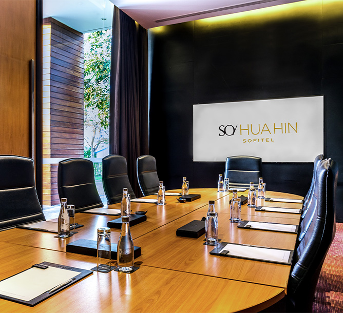 A modern conference room with a long wooden table, black leather chairs, notepads, and water bottles. The atmosphere is professional and well-lit.