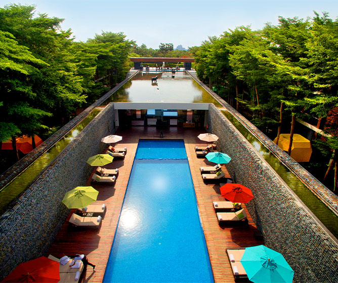 Luxurious resort pool scene with vibrant umbrellas and lounge chairs, surrounded by lush green trees, creating a serene and inviting atmosphere.