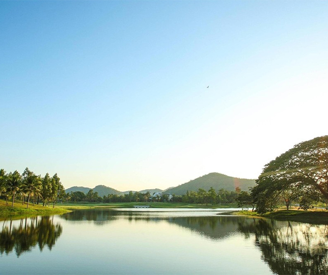 A serene lake reflects a clear blue sky, surrounded by lush greenery and distant hills, creating a peaceful and tranquil landscape.