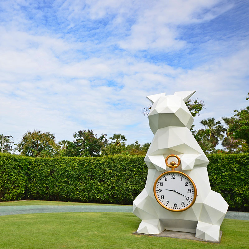 A large white rabbit sculpture holding a clock stands on a green lawn