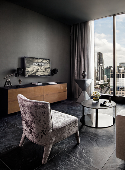 A hotel room living space with a large couch, cushioned chair, small coffee table and mounted flatscreen TV. Floor to ceiling windows display a beautiful skyline view.