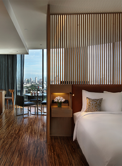 An open, wood themed hotel room. A wooden slatted wall separates a large bed and a small dining arean