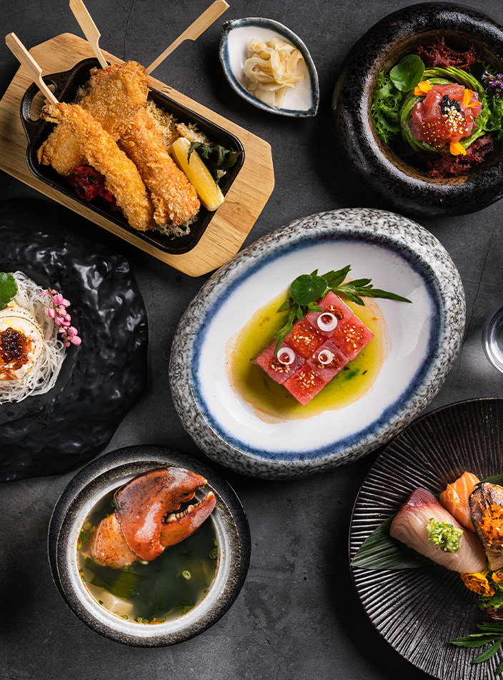A selection fish, sushi and dessert dishes presented on a vareity of different plates and bowls.