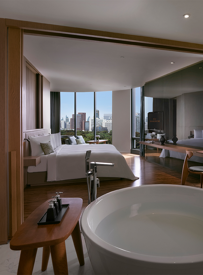 A large open hotel room. A large wooden doorway separates a bathroom with a circular bathtub and a bedroom with a king size bed.