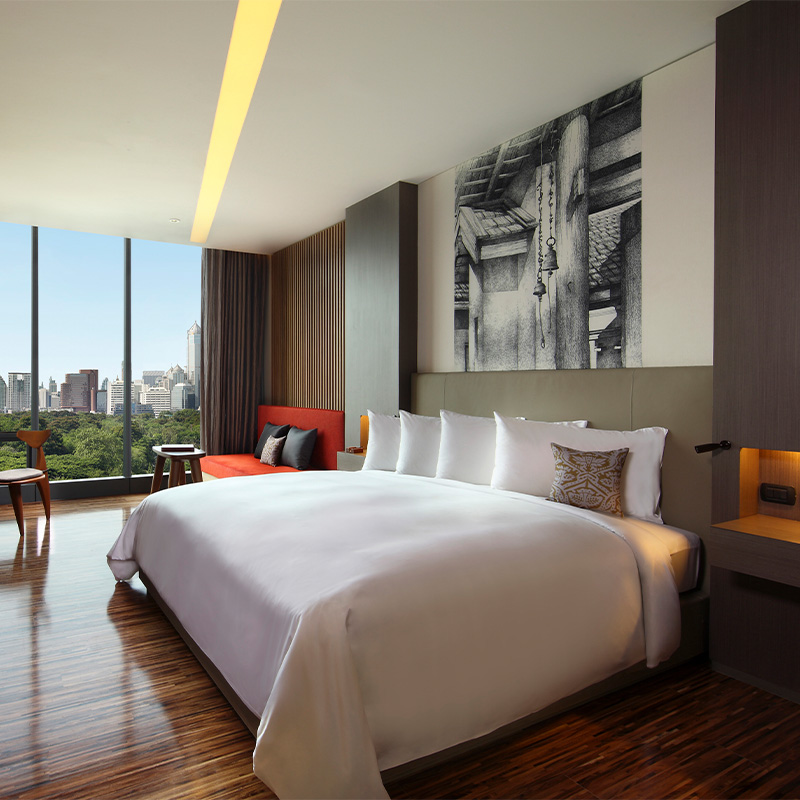 A large wooden themed bedroom with a king sized bed, mounted TV, desk and a floor to ceiling window.