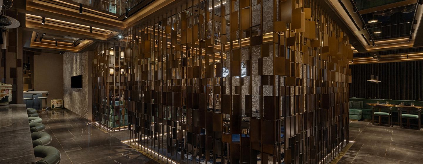 Contemporary restaurant interior with dim lighting, featuring a striking wall of vertical wooden panels. Cozy seating and warm tones create an inviting atmosphere.
