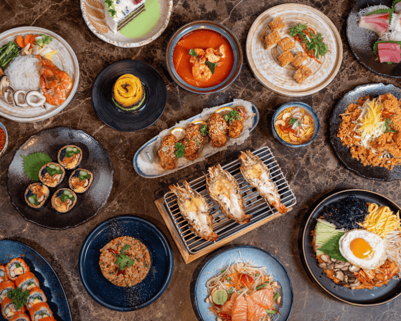 http://A%20colorful%20bird's-eye%20view%20of%20a%20diverse%20Asian%20feast%20on%20a%20dark%20marble%20table,%20displaying%20Tom%20Yum%20soup,%20grilled%20giant%20river%20prawns,%20sushi%20rolls,%20Pad%20Thai,%20and%20various%20side%20dishes.