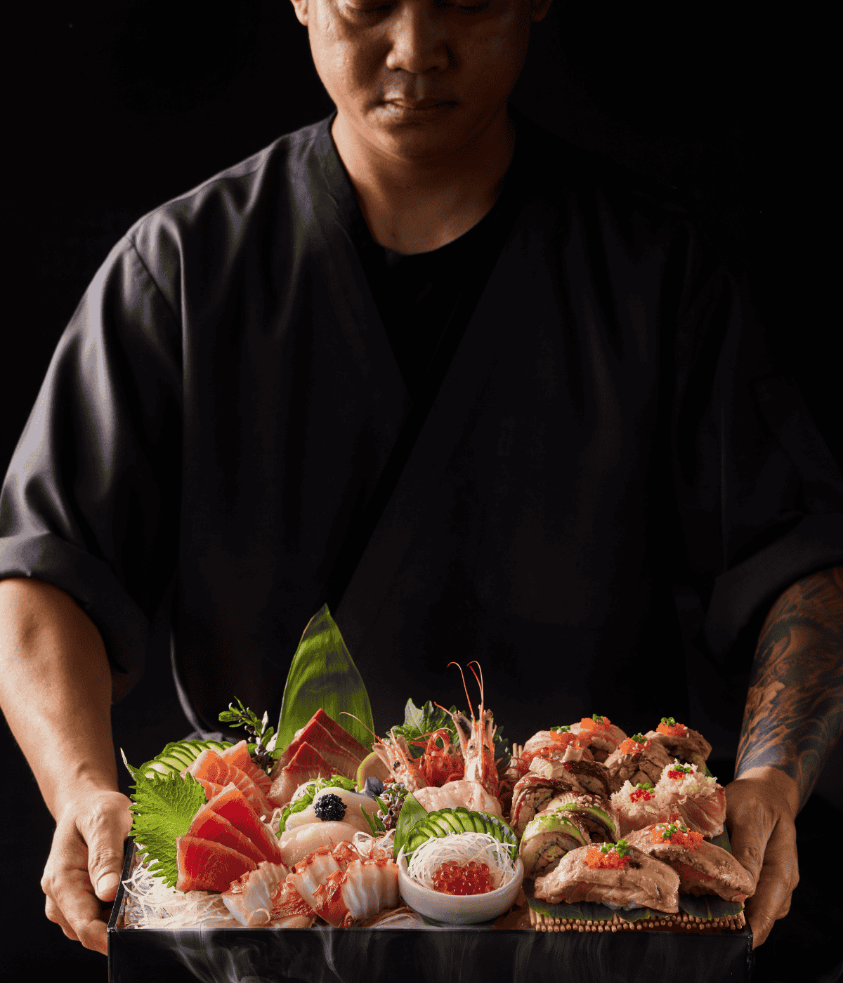 A professional sushi chef in dark uniform presenting an exclusive, steaming platter of fresh sashimi, salmon, caviar, and artfully prepared sushi rolls.