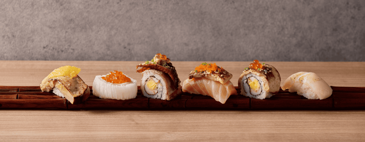 Six exquisite premium sushi creations garnished with salmon, caviar, and delicate toppings, lined up on a dark wooden board.