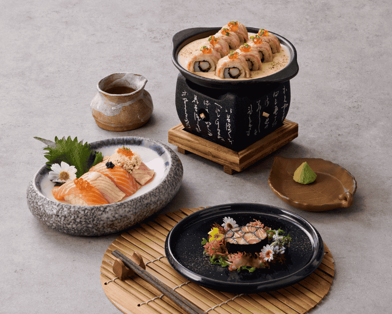 http://A%20premium%20Japanese%20dinner%20set%20showcasing%20a%20small%20clay%20hot%20pot%20with%20sushi%20rolls%20in%20a%20creamy%20sauce,%20seared%20salmon%20nigiri,%20and%20a%20beautifully%20arranged%20mosaic%20sushi%20roll%20decorated%20with%20edible%20flowers.