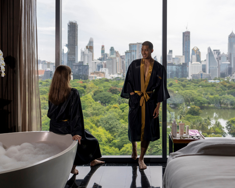 http://Close-up%20profile%20of%20a%20smiling%20woman%20in%20a%20black%20and%20gold%20robe%20sitting%20next%20to%20a%20white%20freestanding%20bathtub%20in%20a%20luxurious%20spa%20room%20with%20a%20city-view%20window.%20