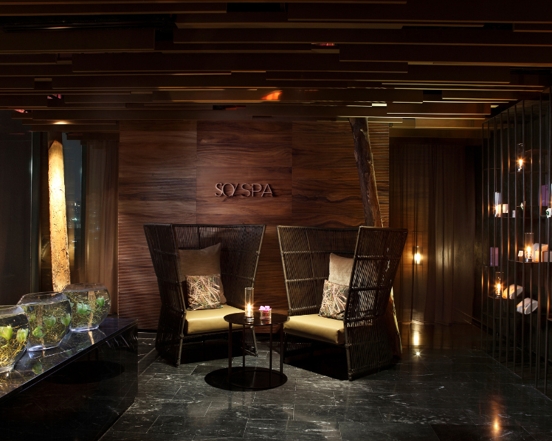 http://Intimate%20waiting%20area%20at%20SO/%20SPA%20featuring%20two%20high-backed%20woven%20armchairs,%20low%20tables%20with%20candles,%20warm%20wooden%20paneling,%20and%20candlelit%20glass%20bowls%20on%20a%20black%20marble%20counter.%20
