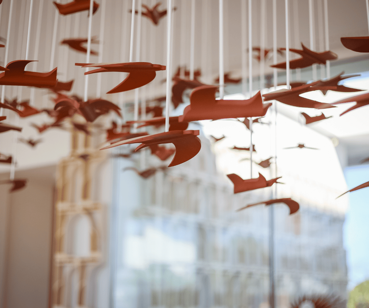 Un groupe d'oiseaux en papier rouge suspendus au plafond, créant une atmosphère fantaisiste et aérienne dans un espace lumineux et moderne.