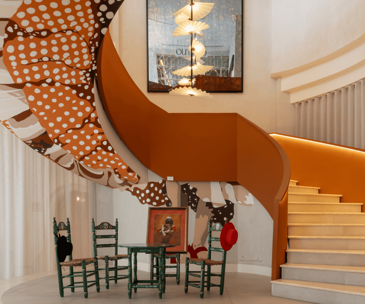 Un intérieur élégant avec un escalier en colimaçon, des œuvres d'art colorées aux murs, une table verte avec des chaises et un portrait encadré. Un éclairage chaleureux rehausse le décor.