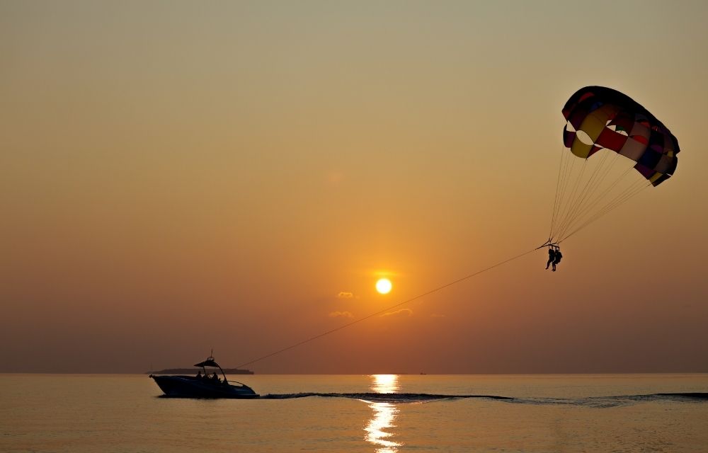 http://Two%20persons%20enjoying%20parasailing%20during%20sunset,%20with%20the%20sun%20setting%20behind%20them%20and%20casting%20warm%20colors%20across%20the%20sky.
