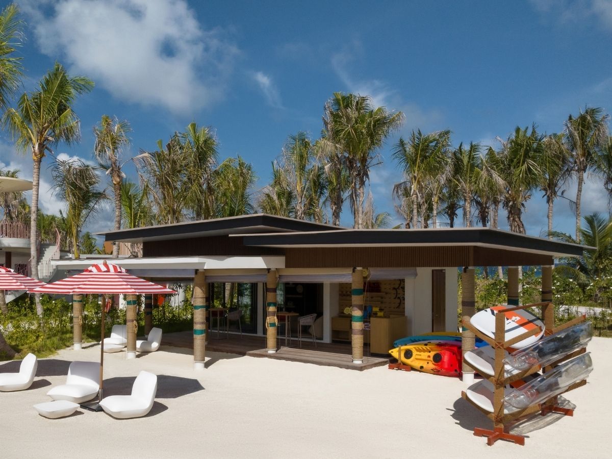 A beach house with vibrant umbrellas, lounge chairs and paddle boards arranged on the sandy beach.