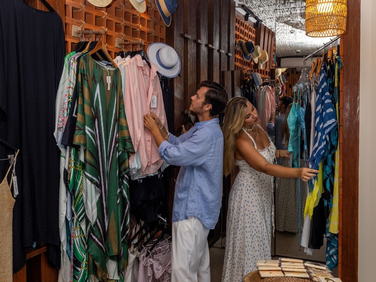 A man and woman shopping together, looking at clothes on racks in a clothing store.