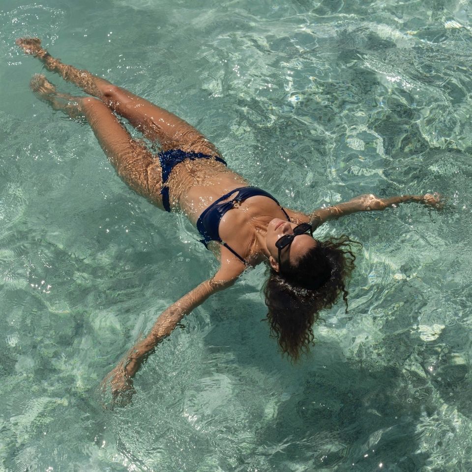 A woman in a bikini leisurely floats on her back in calm water.