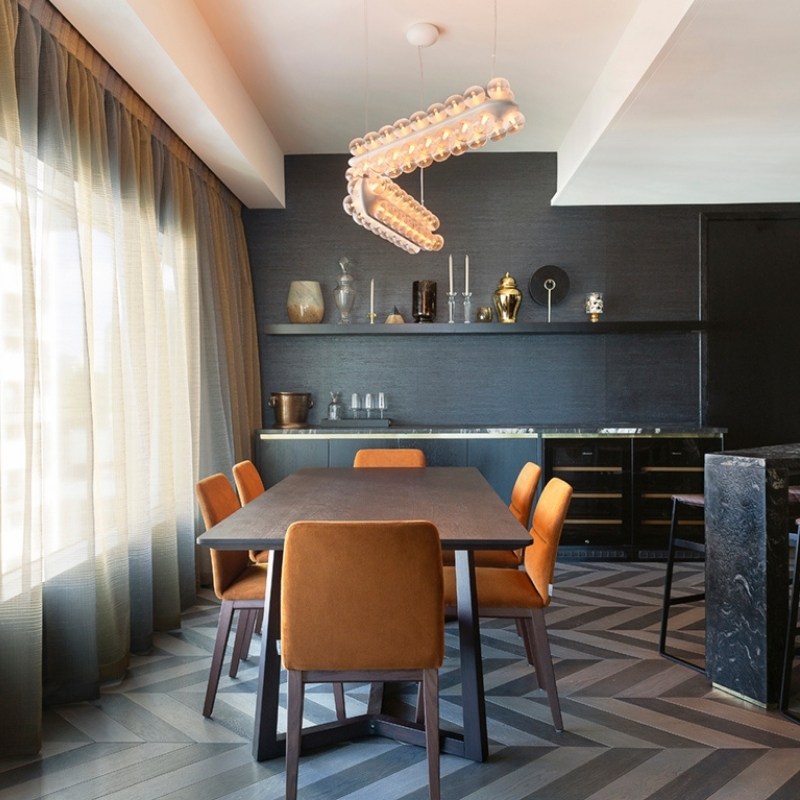 http://Modern%20dining%20area%20featuring%20a%20sleek%20table,%20plush%20orange%20chairs,%20a%20striking%20light%20fixture,%20and%20minimalist%20decor%20against%20dark%20walls.