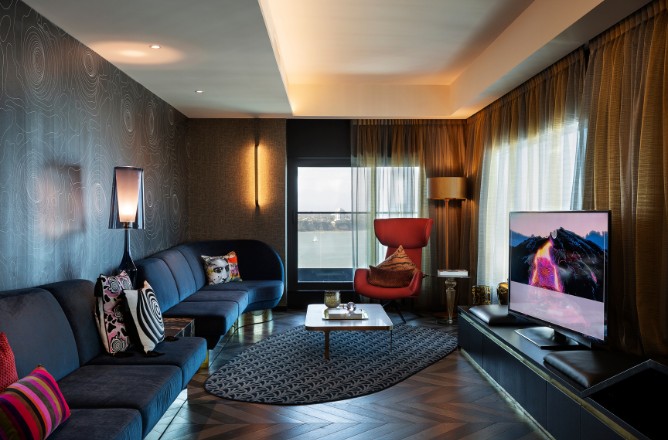 http://Modern%20living%20room%20with%20a%20curved%20blue%20sofa,%20red%20accent%20chair,%20stylish%20decor,%20large%20window,%20and%20a%20sleek%20television%20on%20a%20dark%20media%20unit.