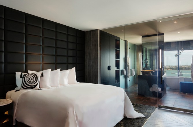 http://Luxurious%20hotel%20room%20featuring%20a%20king%20bed%20with%20plush%20white%20linens,%20stylish%20black%20accent%20wall,%20and%20a%20glass-walled%20bathroom.