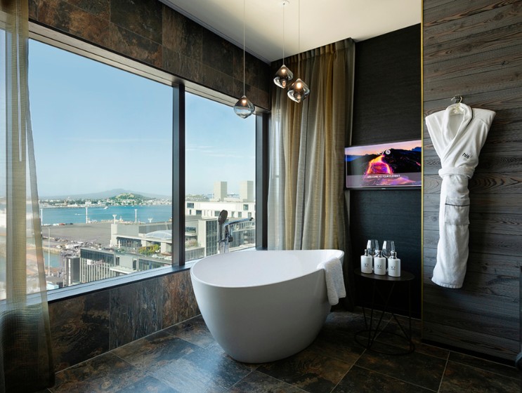 Elegant bathroom featuring a freestanding tub, stunning bay view, modern decor, and a TV, with a plush robe hanging nearby.
