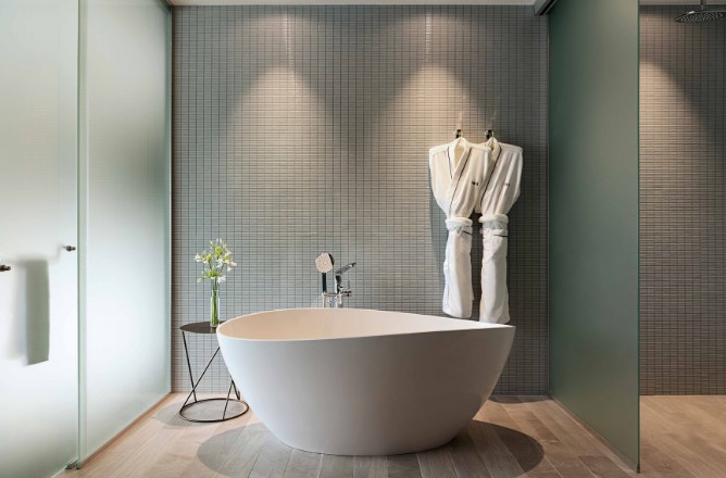 http://A%20modern%20bathroom%20featuring%20a%20sleek%20white%20freestanding%20tub,%20green%20wall,%20glass%20shower,%20stylish%20stool,%20and%20hanging%20bathrobes.